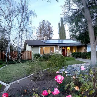 A suburban house with a well-maintained garden featuring blooming flowers and solar panels on the roof.