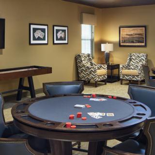 A cozy game room featuring a poker table with cards and chips, surrounded by comfortable chairs and decorated with artwork on the walls.