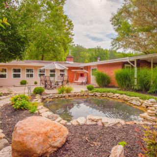 A tranquil garden with a pond in front of a house surrounded by lush greenery.