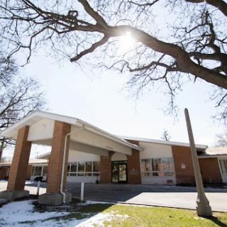 A modern building basking in sunlight with snow on the ground and trees framing the scene.