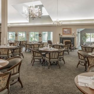 An elegantly designed dining room with multiple tables and chairs, featuring a chandelier and carpeted flooring.