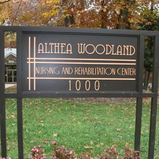 A sign for the Althea Woodland Nursing and Rehabilitation Center set in a grassy area with fall foliage.