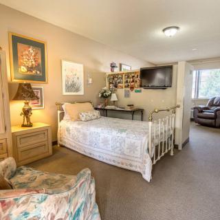 A cozy bedroom featuring a single bed, artwork on the walls, and a TV mounted on the wall.