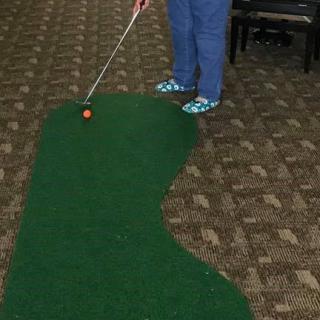 Person playing mini golf indoors on a small putting green.