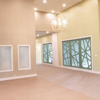 A spacious and modern living room featuring high ceilings, a chandelier, and decorative windows.
