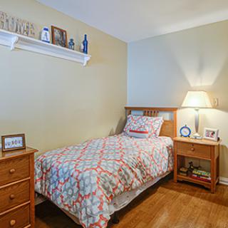 A cozy bedroom with a single bed and warm lighting, featuring wooden furniture and decorative elements.
