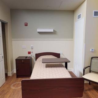 A simple hospital room with a single bed, nightstand, and chair.