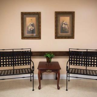 A waiting area with two metal benches, a small wooden table with a plant, and framed paintings on the wall.