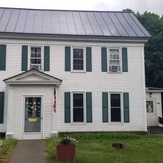 A white house with green shutters and a small American flag by the entrance.