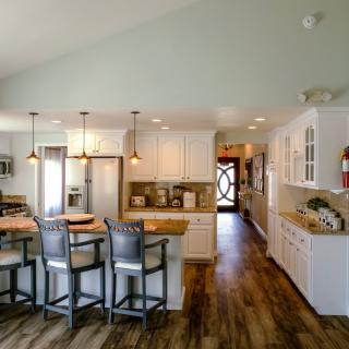 A modern kitchen with white cabinets, pendant lighting, and wooden flooring.