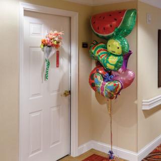 A hallway with a decorated door featuring a bouquet of flowers and colorful balloons.