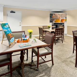 A cozy room set up for an art class, featuring tables with art supplies, easels displaying artwork, and a television in the background.