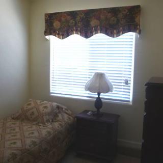 A cozy bedroom with a bed, nightstand, lamp, and a window with blinds.
