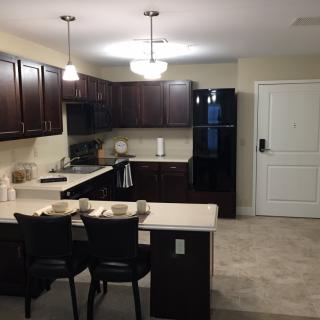 A modern kitchen with dark cabinets, a small dining area, and pendant lighting.