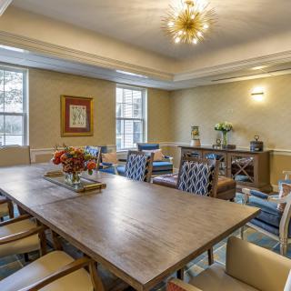 A stylish dining room featuring a large wooden table surrounded by chairs, illuminated by an elegant chandelier.