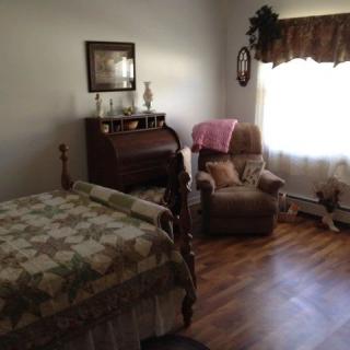 A cozy bedroom with wooden flooring, featuring a bed, recliner chair, and a desk by the window.