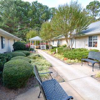 A serene garden pathway with benches, surrounded by lush greenery and trees.