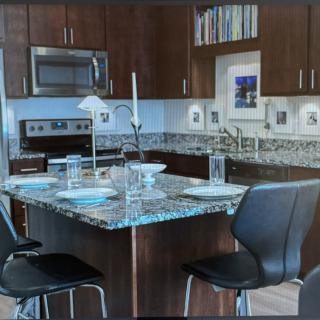 A modern kitchen with granite countertops and dark cabinets, featuring a stove, microwave, and bar stools.