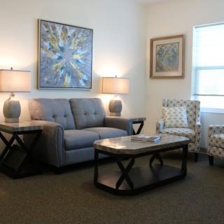 A cozy living room with a sofa, armchairs, and a coffee table, complemented by artwork on the walls and warm lighting from lamps.