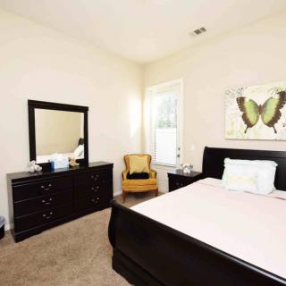 A neatly arranged bedroom with a bed, dresser, mirror, and artwork.
