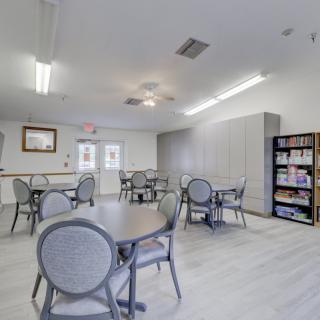 A community room with tables, chairs, and a bookshelf under bright lighting.