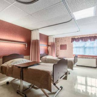 A view of a hospital patient room featuring two beds and natural light from a window.