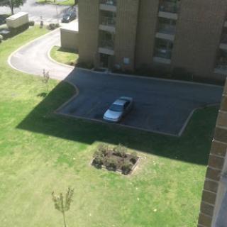 A view from above showing a parked car in a lot surrounded by grass and a building.