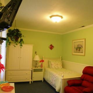 A cozy bedroom with green walls, featuring a single bed, a red chair, and a white wardrobe.