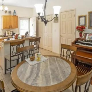 A cozy dining area with a round table, wooden chairs, and a view into the kitchen, featuring a vintage piano in the corner.