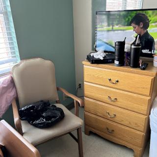 A cozy room featuring a chair, dresser, and a television displaying a scene.