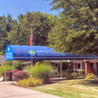 A welcoming view of the front entrance to a community center, featuring lush greenery and a blue awning.
