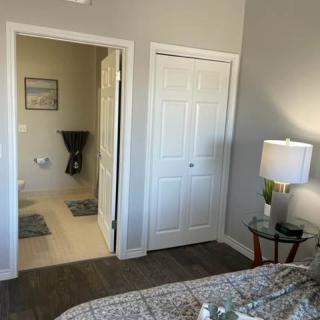 A cozy bedroom with a bed, nightstand, lamp, and a view into an adjoining room through an open doorway.