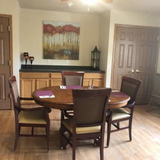 A dining room featuring a round wooden table with four chairs, a cabinet in the background, and a decorative painting on the wall.