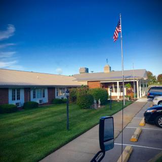 A building with an American flag in front, surrounded by a parking lot and grassy area under a clear blue sky.