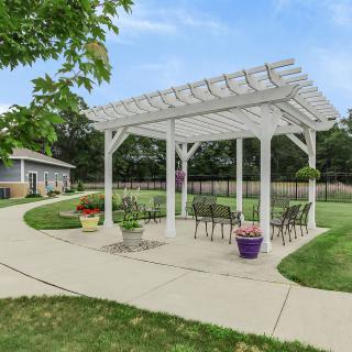A white pergola with seating in a landscaped garden setting.