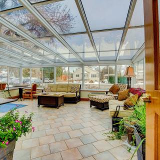 A spacious sunroom with a glass ceiling, furnished with comfortable seating and decorated with plants.