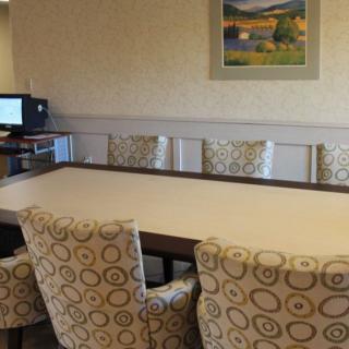 A conference room with a large meeting table surrounded by patterned chairs, a computer in the corner, and a landscape painting on the wall.