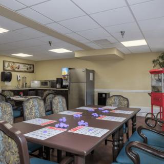 A dining area with a kitchen setup, featuring tables and chairs, a refrigerator, and a popcorn machine.