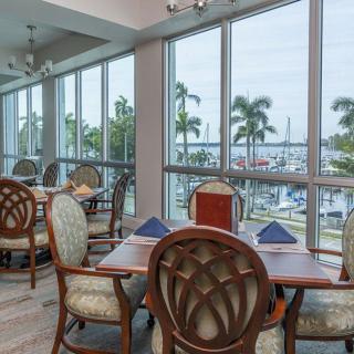 A well-lit restaurant dining area with large windows offering a view of palm trees and the outdoors.
