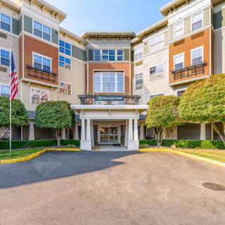 A view of a multi-story residential apartment building with a landscaped entrance and an American flag displayed outside.