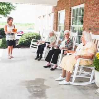 A group of seniors relaxing on a porch in rocking chairs, enjoying each other's company.
