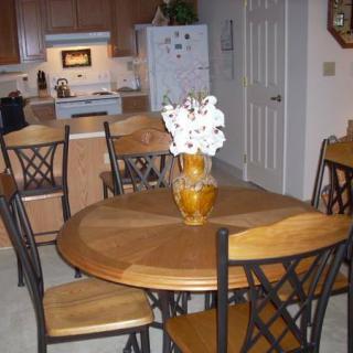A cozy kitchen dining area with a wooden table and chairs, featuring a vase of flowers.