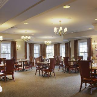 An elegant dining room with neatly arranged tables and chairs, illuminated by chandeliers.
