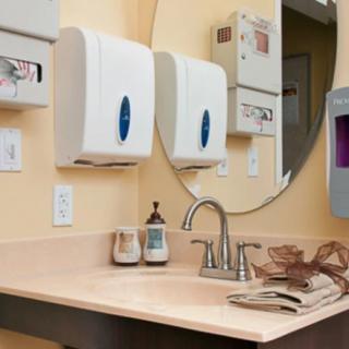 A clean bathroom sink area with a mirror, soap dispenser, and paper towel dispensers.