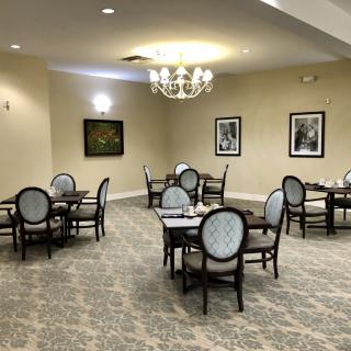 A well-lit dining room with elegant tables and chairs, featuring a chandelier and framed artwork on the walls.