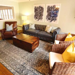 A cozy living room featuring a sofa, armchair, rattan chairs with yellow cushions, and a wooden coffee table, adorned with wall artwork.
