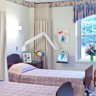 A hospital room with two beds and medical equipment, decorated with a flower vase by the window.