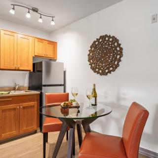 A modern kitchen and dining area with wooden cabinetry, stainless steel appliances, and a stylish glass-top table accompanied by two orange chairs.