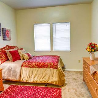 A cozy bedroom with colorful bedding, two windows, and wooden furniture.