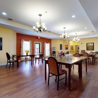 A spacious dining area with wooden floors, decorated with chandeliers and arranged with tables and chairs.